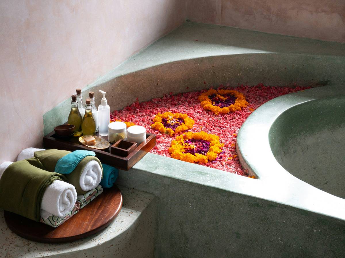 bath and body perfume oil poured into warm bathwater with dried lavender buds floating nearby